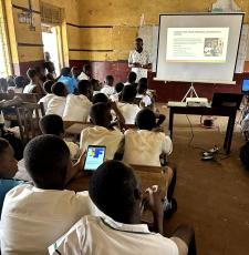 A librarian teaches school students in a school classroom online safety skills, using a whiteboard and projector for slides. 