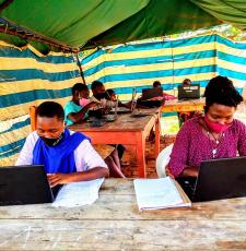 Women and youth learning ICT skills in a tented enclosure at Nyarushanje Community Library.