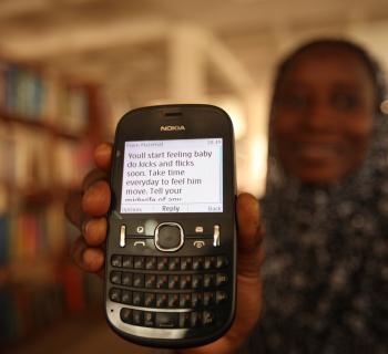 A mother-to-be shows a mobile phone with a text messages advising her about what to expect in pregnancy. 