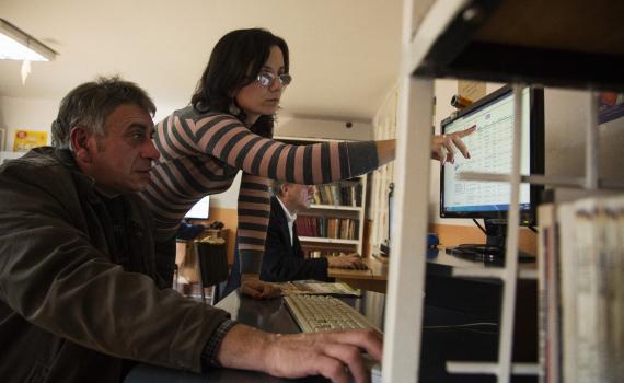 A librarian points out information on a computer screen to a farmer.