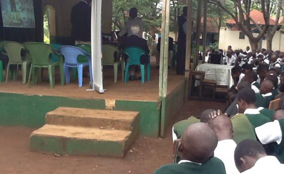 Children taking part in an online inter-school debate. The children are seeing images of the other school on a big screen.