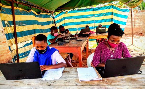 Women and youth learning ICT skills in a tented enclosure at Nyarushanje Community Library.