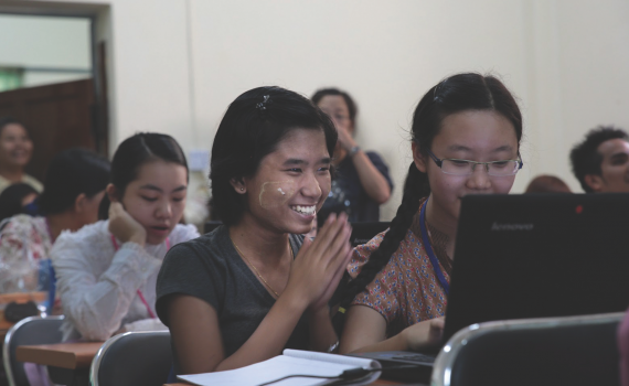 Smiling students learning to use computers in University of Yangon.