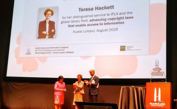 Teresa Hacket receives the award at the IFLA congress. Backdrop is of a banner of Teresa.